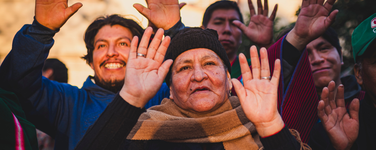Na imagem, consta quatro pessoas com as mãos erguidas no momento da recepção dos primeiros raios do Sol da manhã do dia 21 de junho de 2025, na Praça Kantuta, São Paulo.