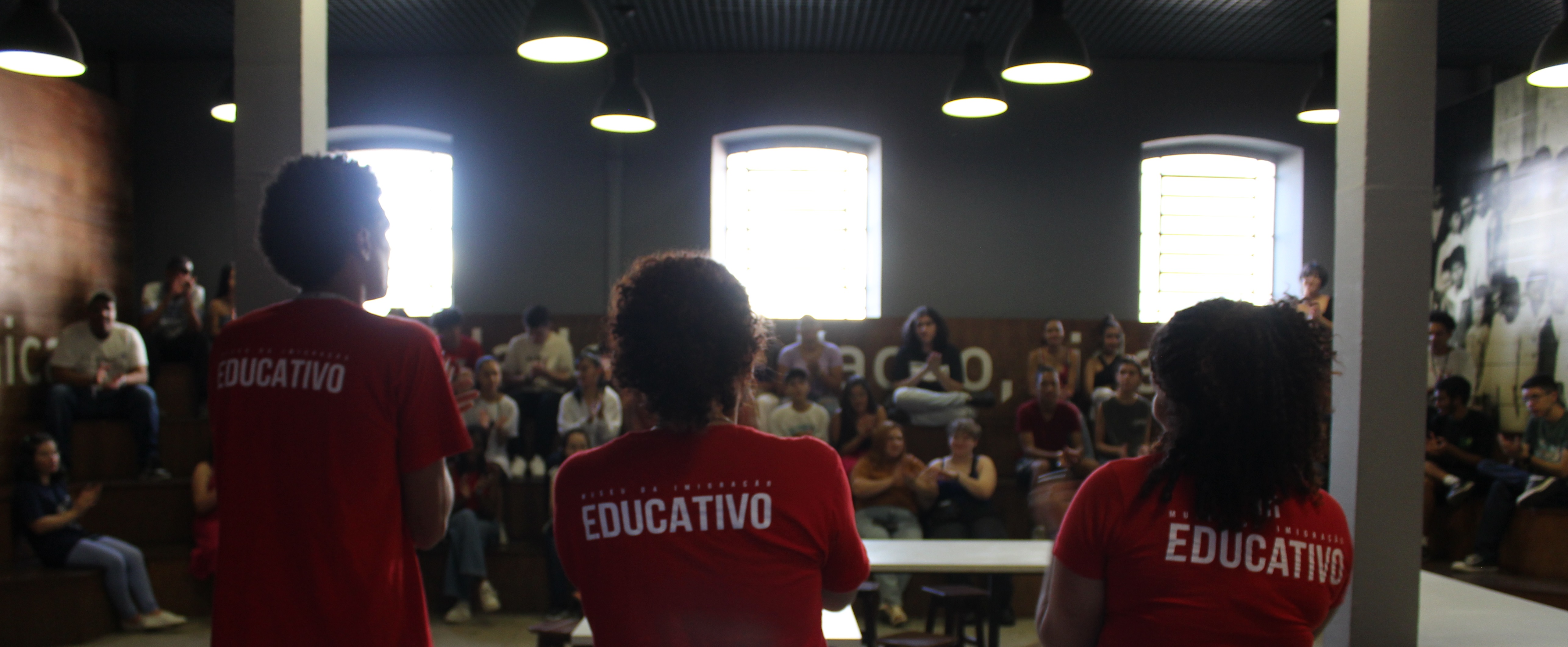 Educadores diante de uma grande plateia, em atividade realizada no espaço educativo do Museu da Imigração.