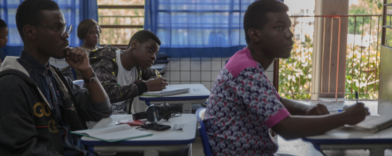 sala de aula com três adultos sentados em carteiras