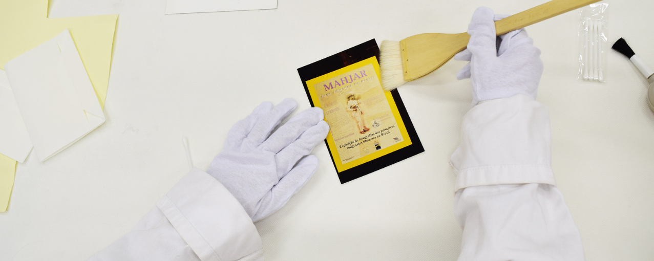 Fotografia de limpeza de acervo, onde aparece um pincel e uma foto.