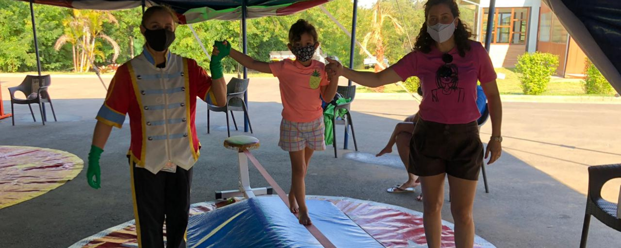 Dois adultos dando apoio a uma criança para se equilibrar em elástico