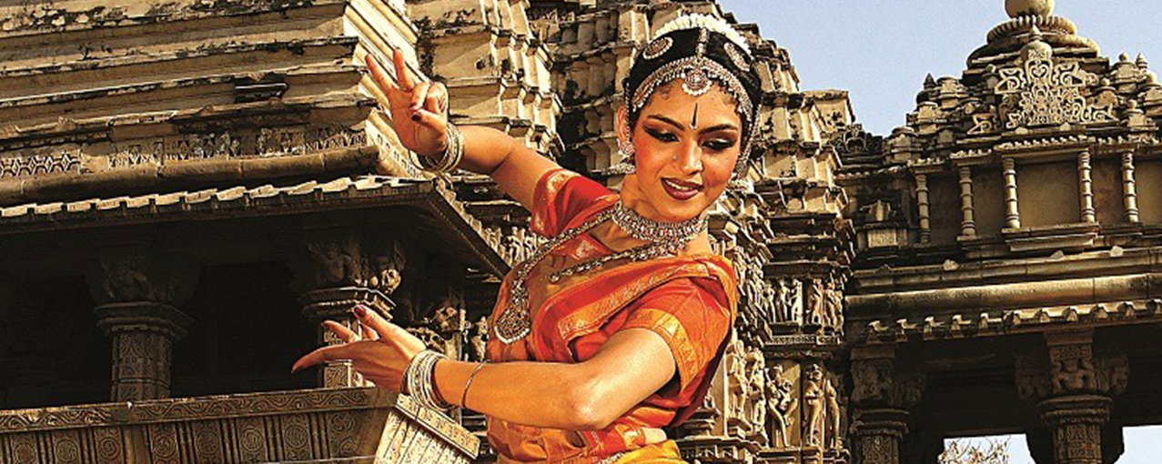 Foto de uma mulher com trajes típicos com pose de dança em frente a monumentos históricos