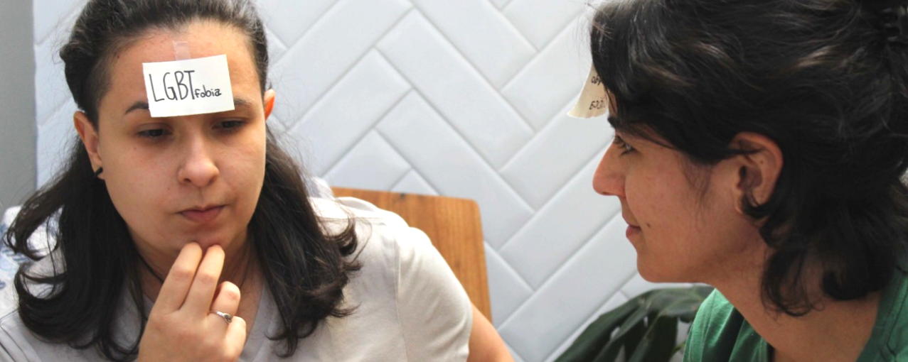 Duas mulheres com pequenos papeis na testa, no jogo Tá na Cara